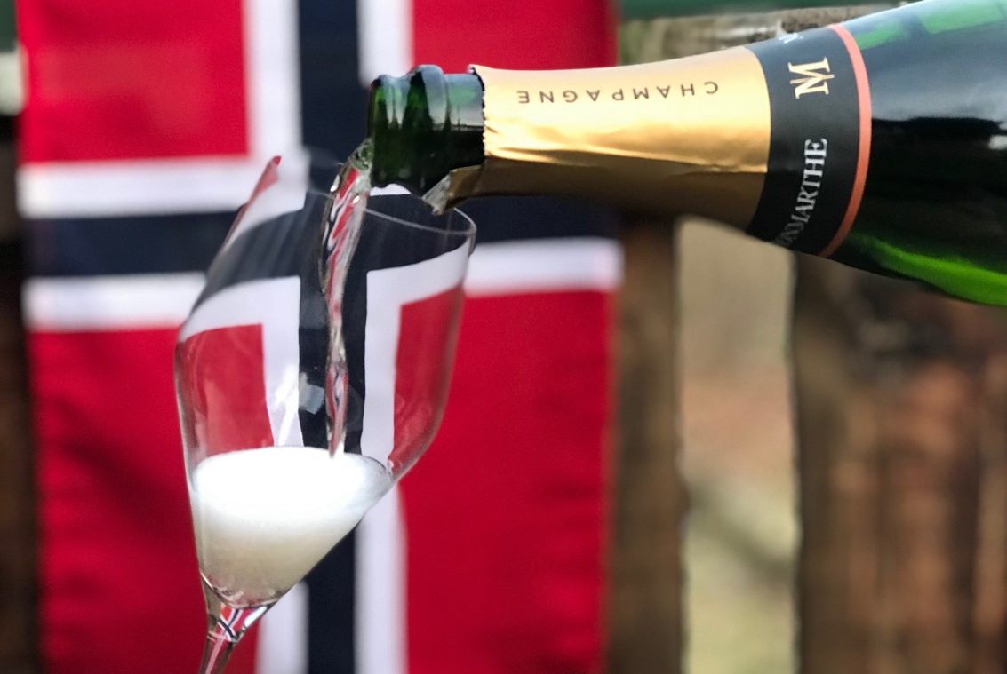 Musserende vin skjenkes i et glass foran det norske flagg.