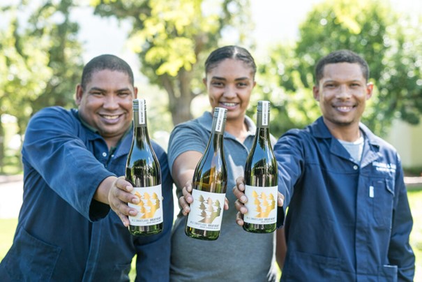 Tre personer holder fram hver sin vinflaske og smiler